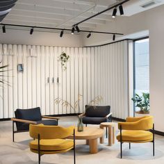 an office lobby with yellow chairs and black tables in front of large windows that have vertical blinds on them