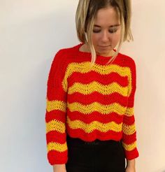 a woman wearing a red and yellow knitted sweater standing in front of a white wall