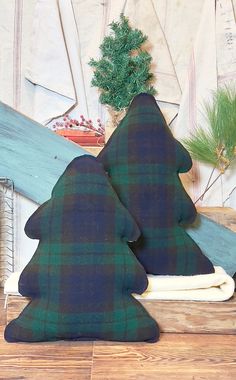 two green and black plaid pillows sitting on top of a wooden table next to a christmas tree