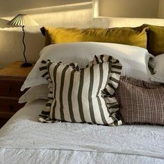 a bed topped with lots of pillows on top of it's headboard next to a night stand