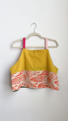 an orange and yellow top hanging on a hanger next to a white wall,