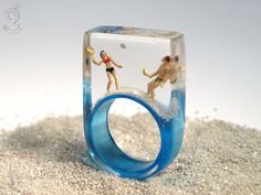 a ring with two figurines in it sitting on sand