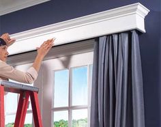 a woman standing on a stepladder in front of a window holding her hands up