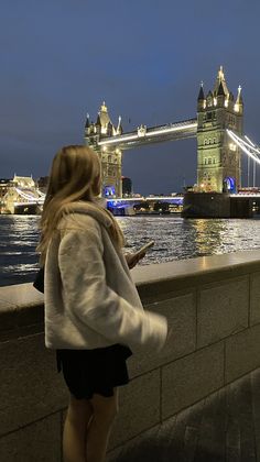 a woman looking at her cell phone in front of the tower bridge and river thames