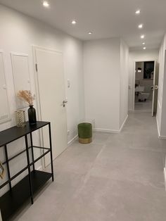 an empty room with white walls and grey flooring is seen in this image, there are two vases on the table