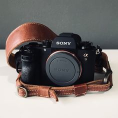 a sony camera sitting on top of a brown leather bag with the strap around it