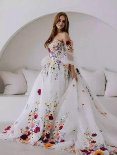 a woman in a white dress with flowers on it standing next to a couch and pillows