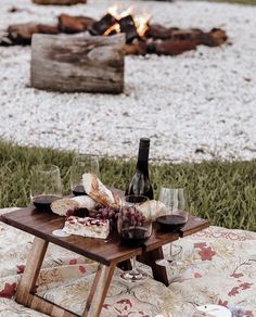 a picnic table with wine, cheese and bread on it in front of an open fire pit