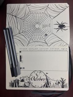 an open notebook with spider webs on it and two black pens next to it