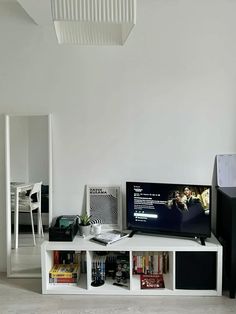 a flat screen tv sitting on top of a white shelf next to a book case