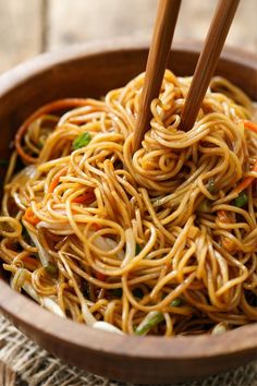 noodles with vegetables and chopsticks in a wooden bowl on top of burloom