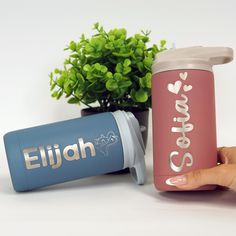 two personalized travel mugs sitting next to each other on a white table with a potted plant in the background