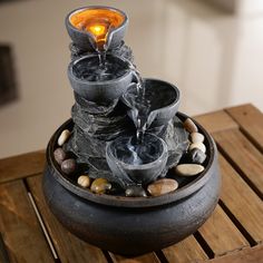 there is a fountain with rocks and water flowing out of it on top of a wooden table