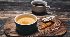 a cup of coffee sitting on top of a wooden table next to spoons and nuts