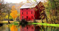 a red house sitting on top of a lush green hillside next to a river filled with water