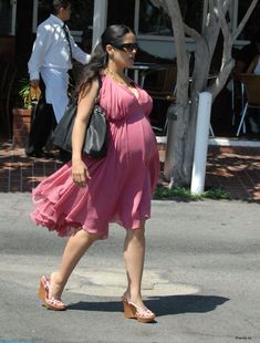 a pregnant woman in a pink dress is walking down the street with her hand on her hip