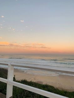 a white fence is near the beach at sunset