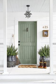 a green front door on a white house with two buckets full of potted plants