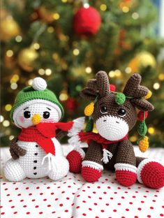 two crocheted stuffed animals sitting next to each other on a table with a christmas tree in the background