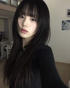 a woman with long black hair and bangs standing in a living room looking at the camera