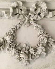 a wreath hanging on the side of a white wall with flowers and leaves around it