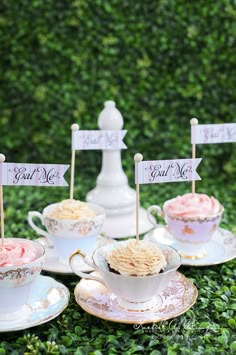 some tea cups and saucers are sitting on the ground with small signs in them