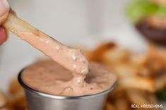 a person dipping some kind of sauce into a small metal cup filled with food items