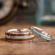 three wedding rings with wood and turquoise inlays on a wooden table next to a clock