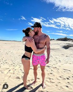 a man and woman in swimsuits standing on the beach with their arms around each other