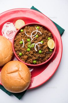 a red plate topped with two sloppy joes next to a bun filled with beans and onions