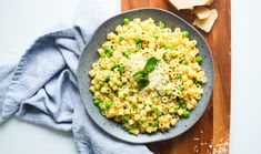 pasta with peas and parmesan cheese in a bowl on a wooden cutting board