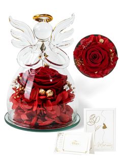 a glass vase filled with red flowers next to a greeting card and an angel figurine