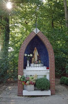 a small shrine in the middle of a park with flowers and plants on it's side