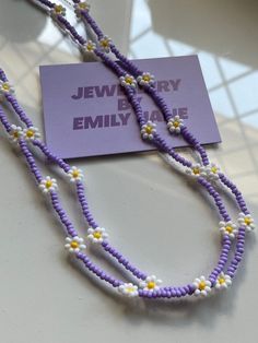 a purple and white beaded necklace on display with a card that says jewelry by emily me