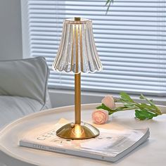 a table lamp sitting on top of a white table next to a book and flowers