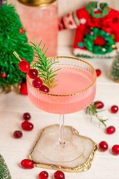 a pink cocktail garnished with fresh cranberries and rosemary sits on a table surrounded by christmas decorations