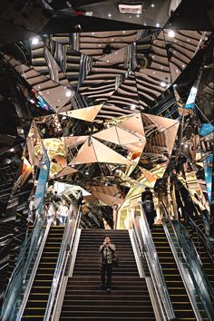 an escalator in a building with mirrors on the ceiling and people walking down it