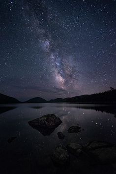 the night sky is filled with stars and milky over a body of water that has rocks in it