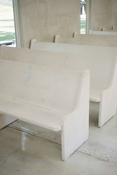 several white benches are lined up in a room with concrete walls and flooring on either side