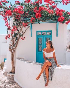 a woman sitting on the side of a building next to a tree with red flowers