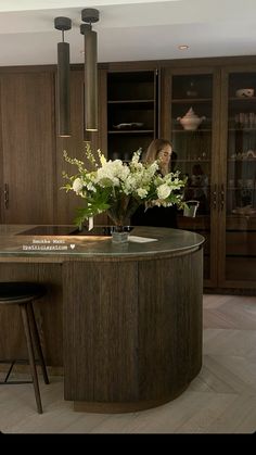 a woman sitting at a kitchen counter with flowers in the center and cabinets behind her