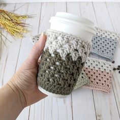 a hand holding a coffee cup with crochet on the side and two cups next to it