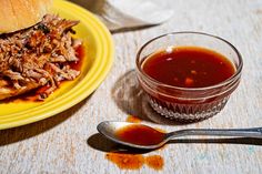 a yellow plate topped with a pulled pork sandwich next to a bowl of bbq sauce