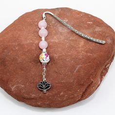 a pink beaded necklace on a rock with a flower charm hanging from it's end