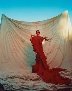 a woman in a red dress is standing on a bed with a large sheet behind her