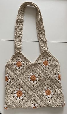 a crocheted bag with orange and white flowers on the front, hanging from a hook