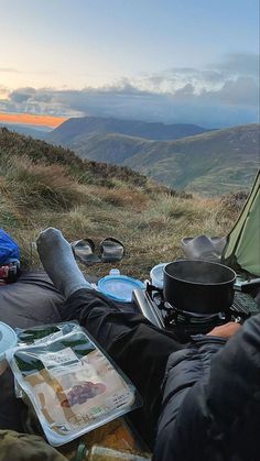 a man laying on top of a grass covered field next to a camping stove and food