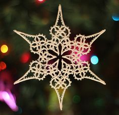 a white snowflake ornament hanging from a christmas tree with colorful lights in the background