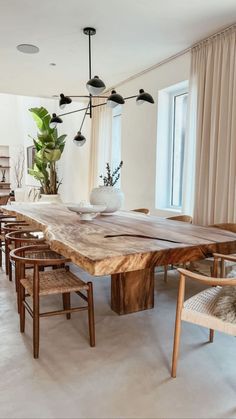 a large wooden table surrounded by chairs in a living room with white walls and windows