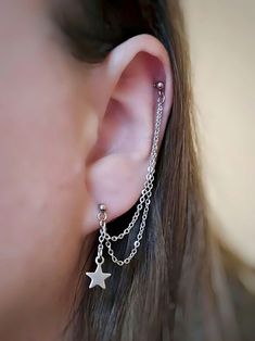 a close up of a person's ear with chain and star earrings on it